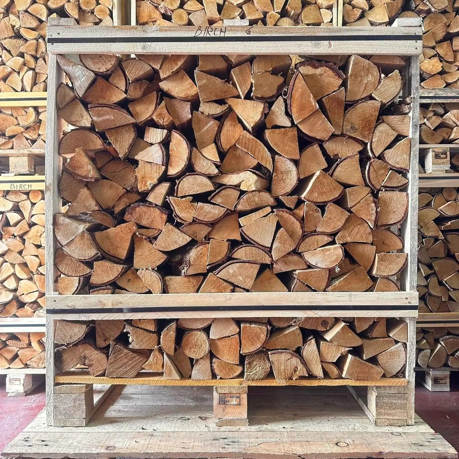 Stack of chopped wood on a wooden pallet with more wood stacked in the background.