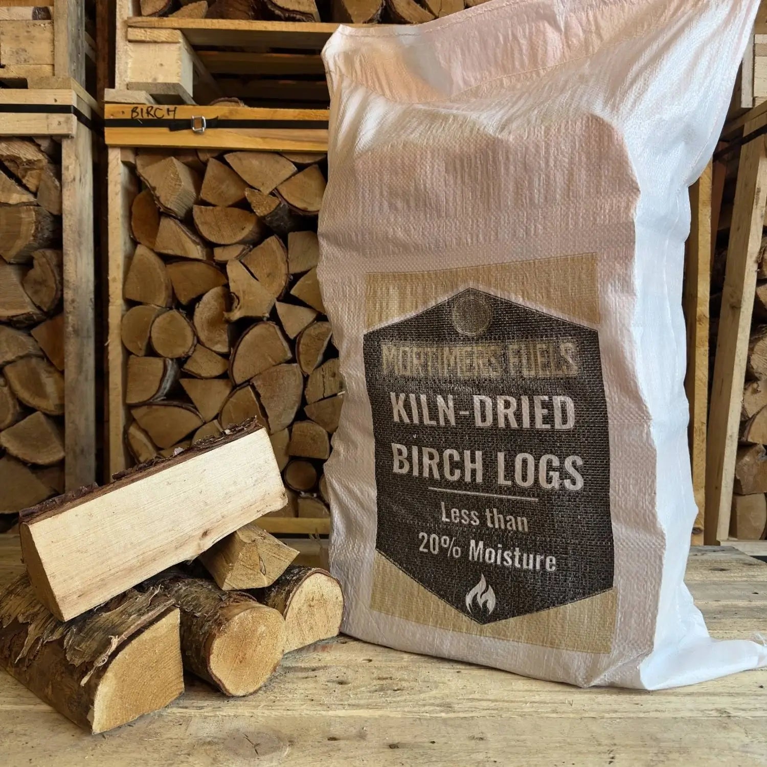 Bag of kiln-dried birch logs with stacked logs in the background