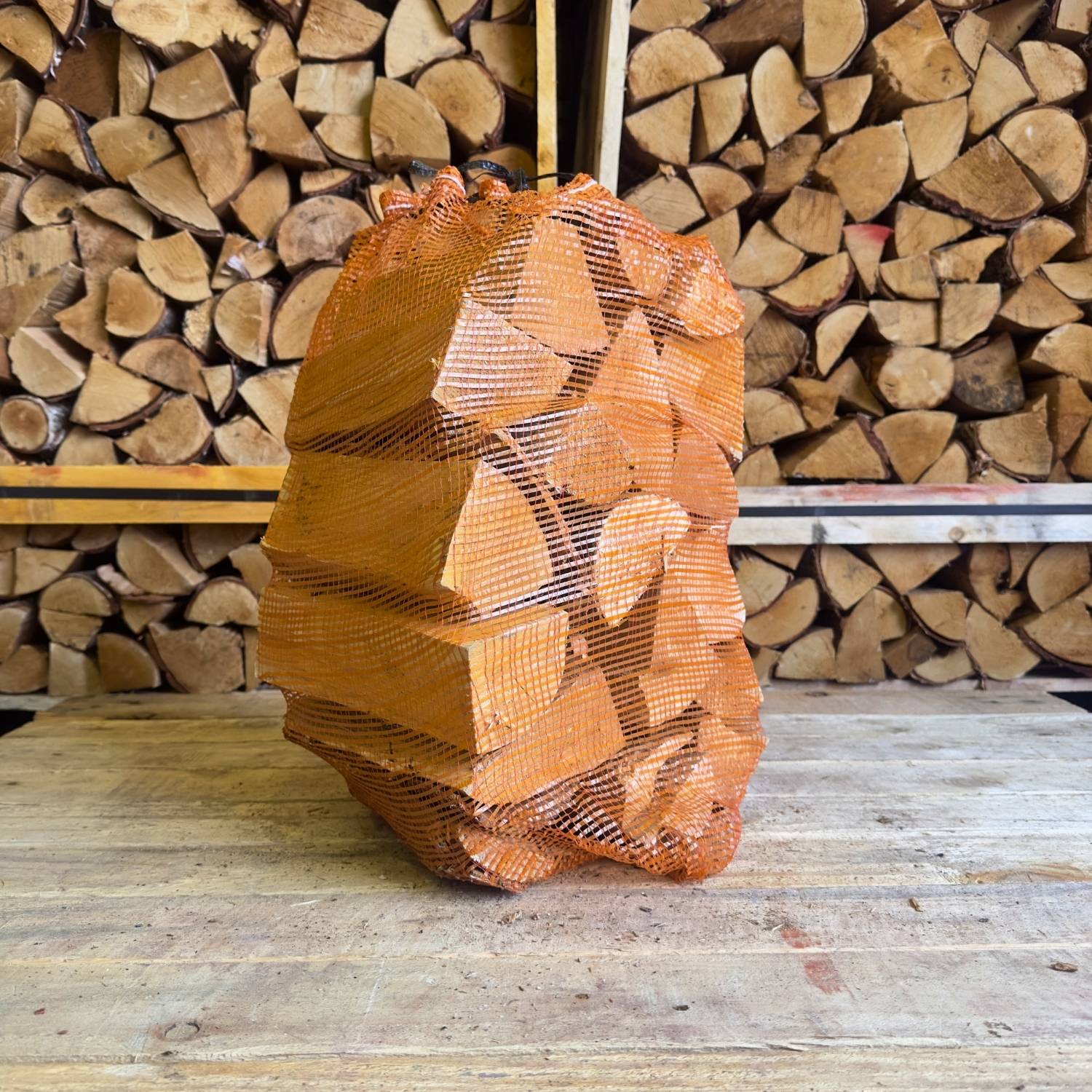 Birch firewood in an orange net with stacked firewood in the background