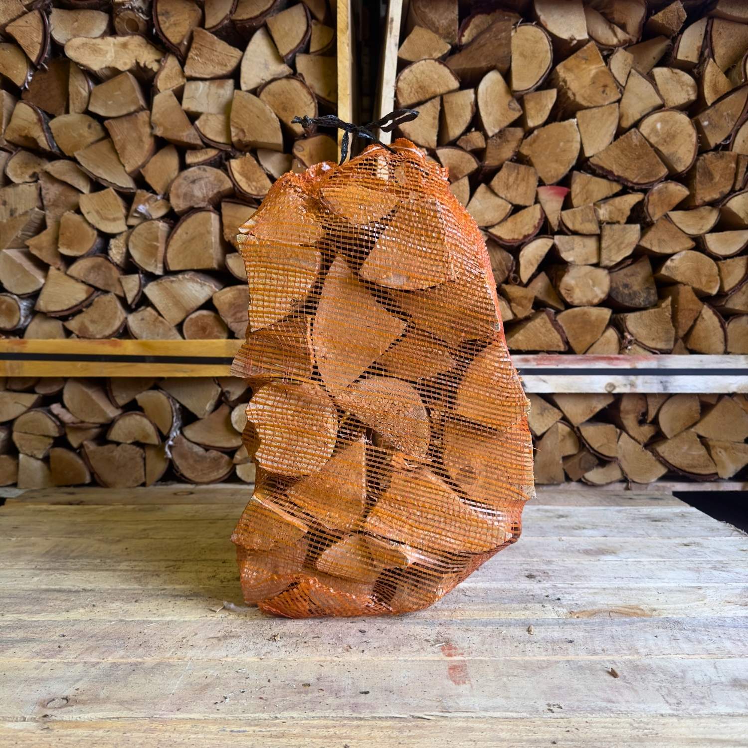 Stack of firewood in a mesh bag with stacked logs in the background