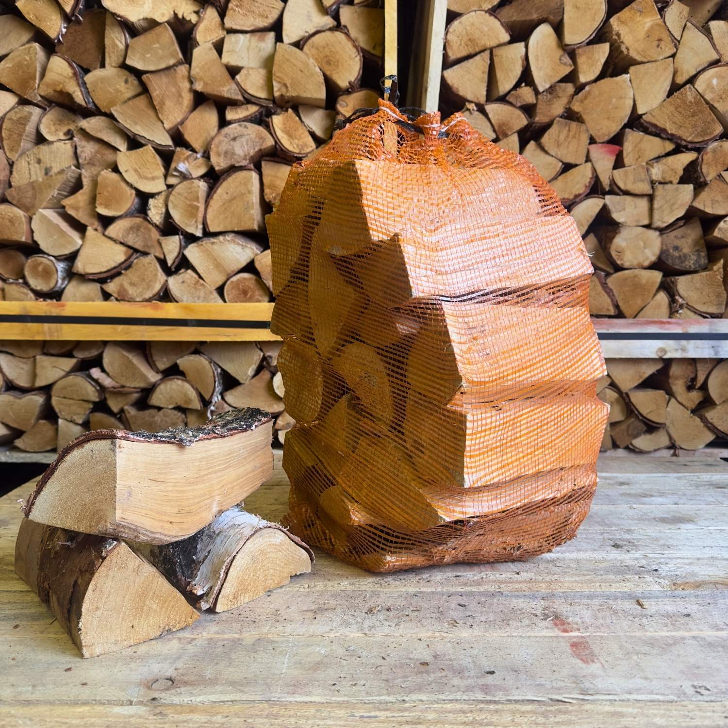 Birch firewood in an orange net with stacked logs in the background