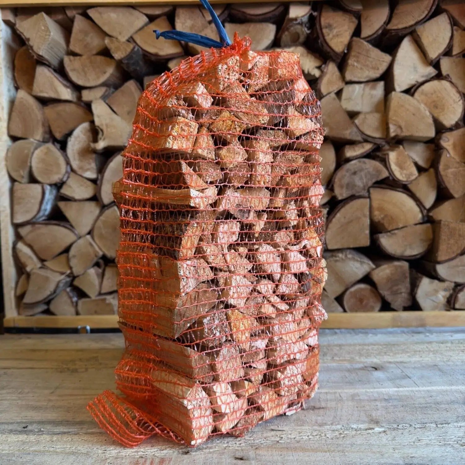 Mesh bag filled with firewood in front of stacked logs