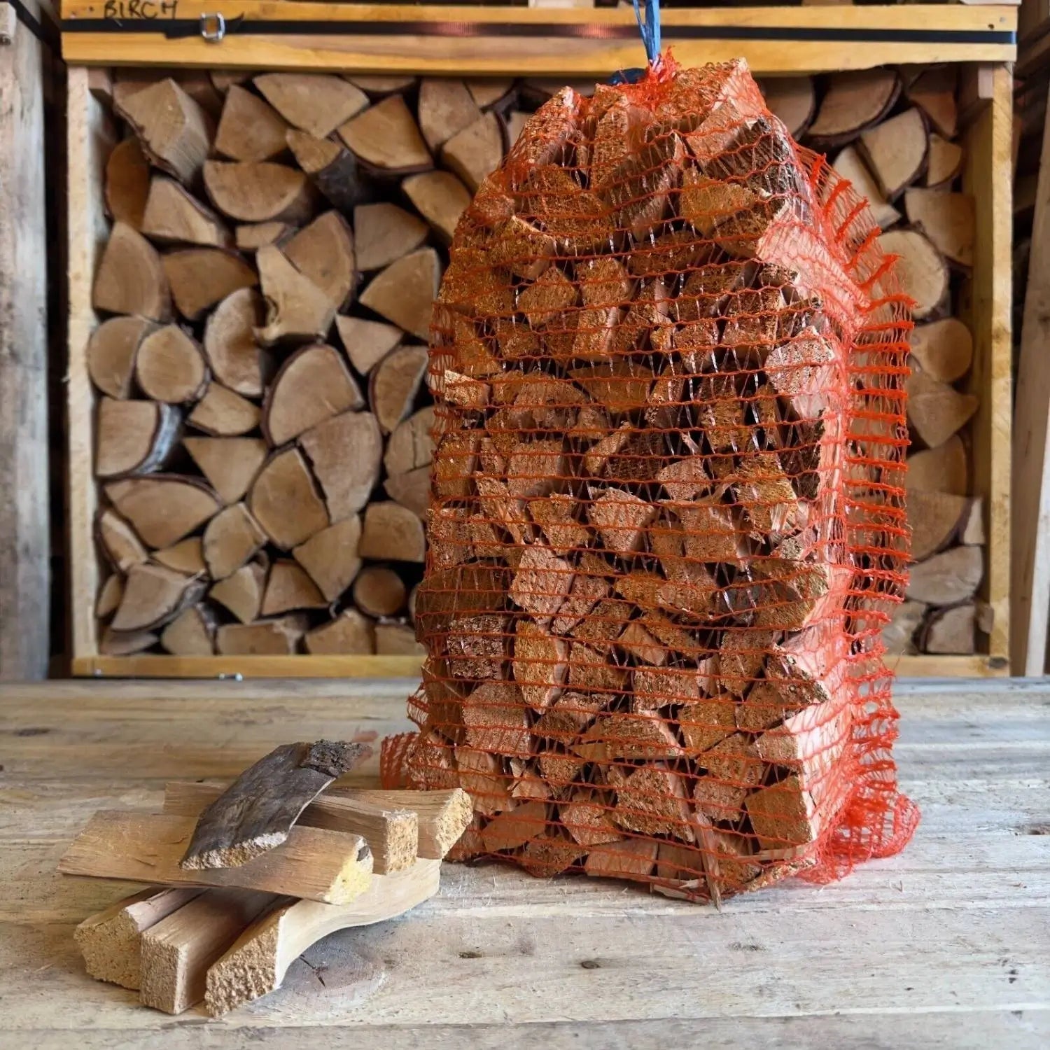 Bag of firewood in front of stacked logs with a axe on a wooden floor.