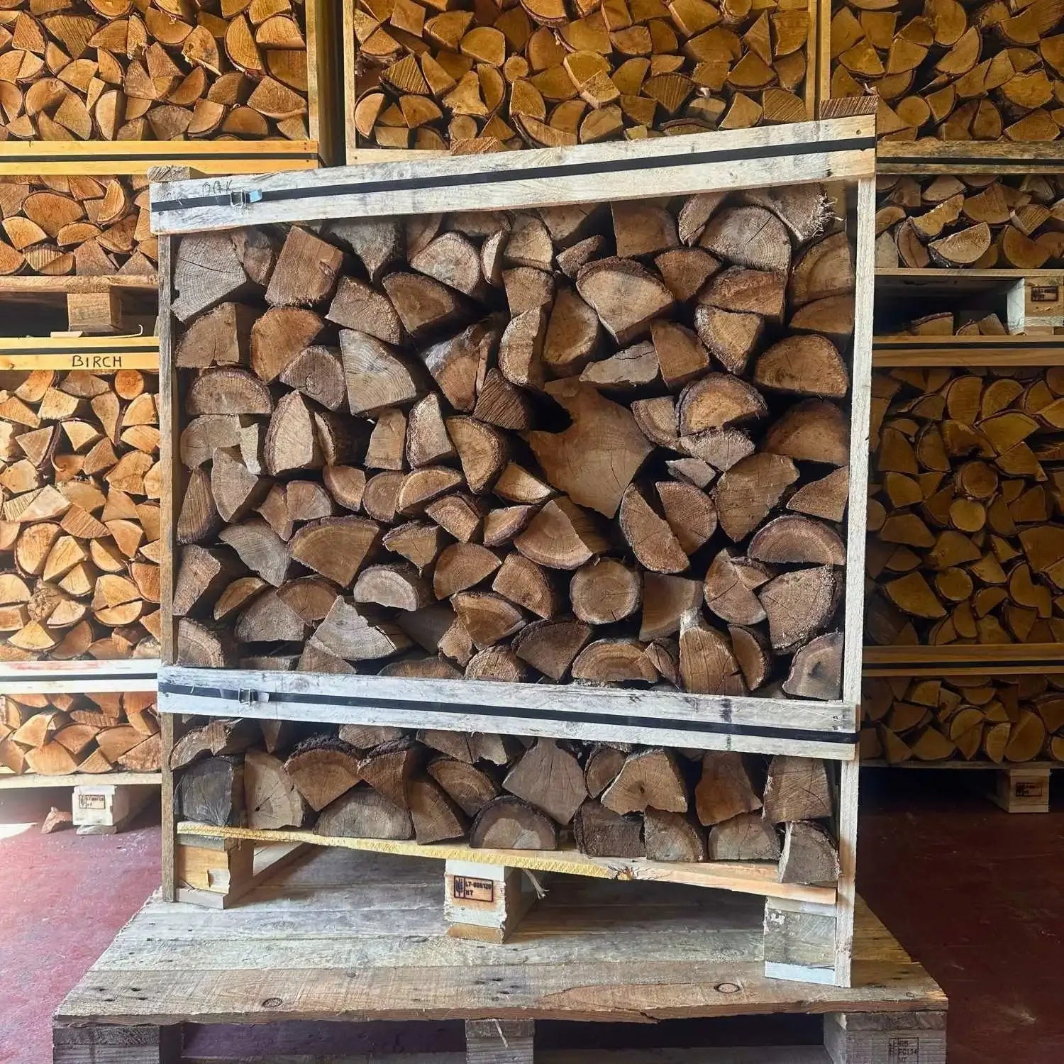 Stack of firewood on a wooden pallet with more firewood stacked in the background.