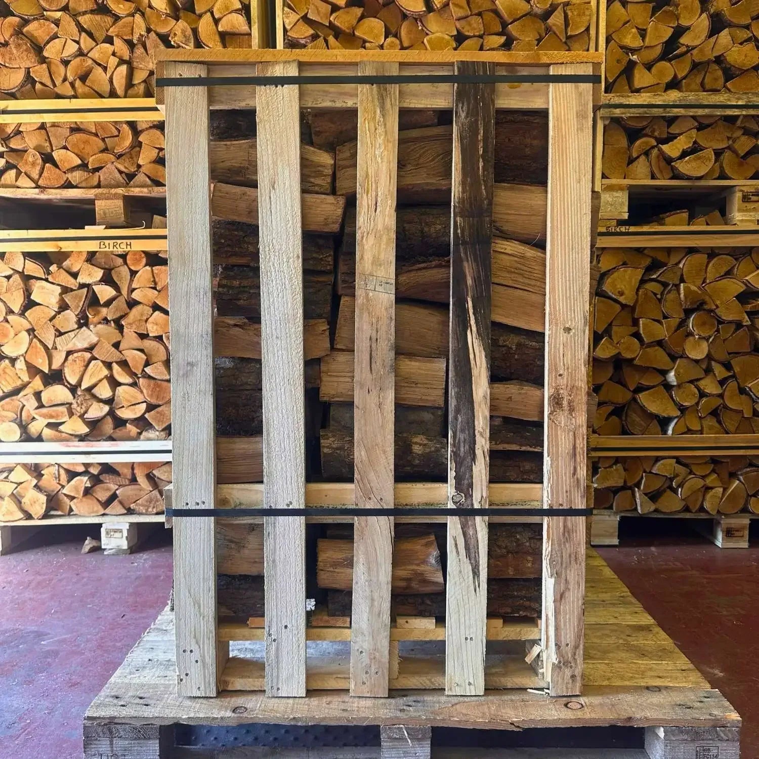 Wooden crate of kiln dried logs against a background of stacked firewood.