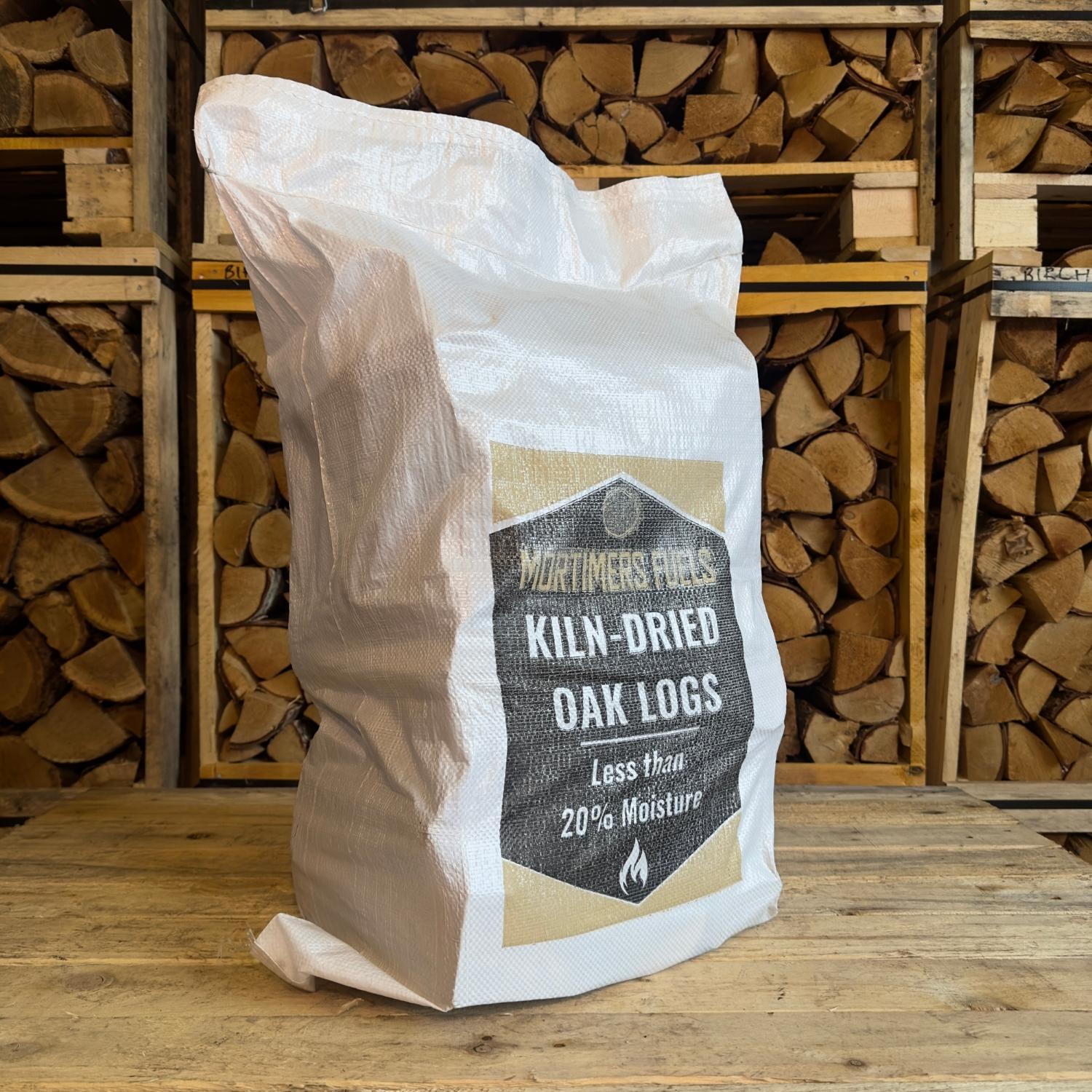 Bag of Mortimer's Fuels kiln-dried oak logs with stacked wood in the background