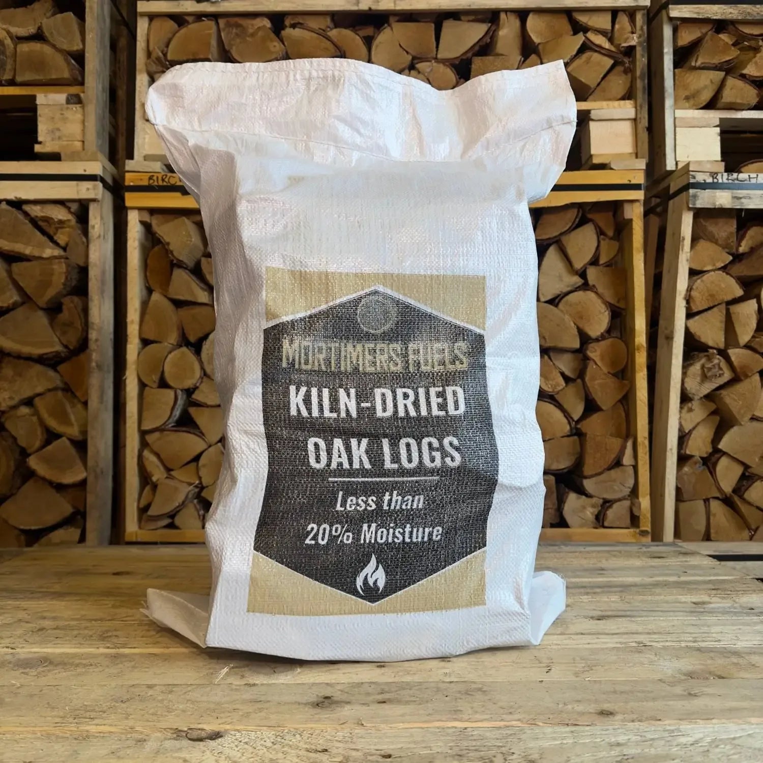 Bag of Mortimer's Fuels Kiln-Dried Oak Logs with stacked logs in the background