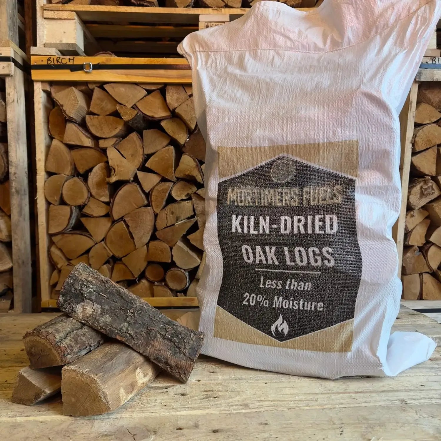 Bag of Mortimer's Fuels Kiln-Dried Oak Logs with stacked logs in the background