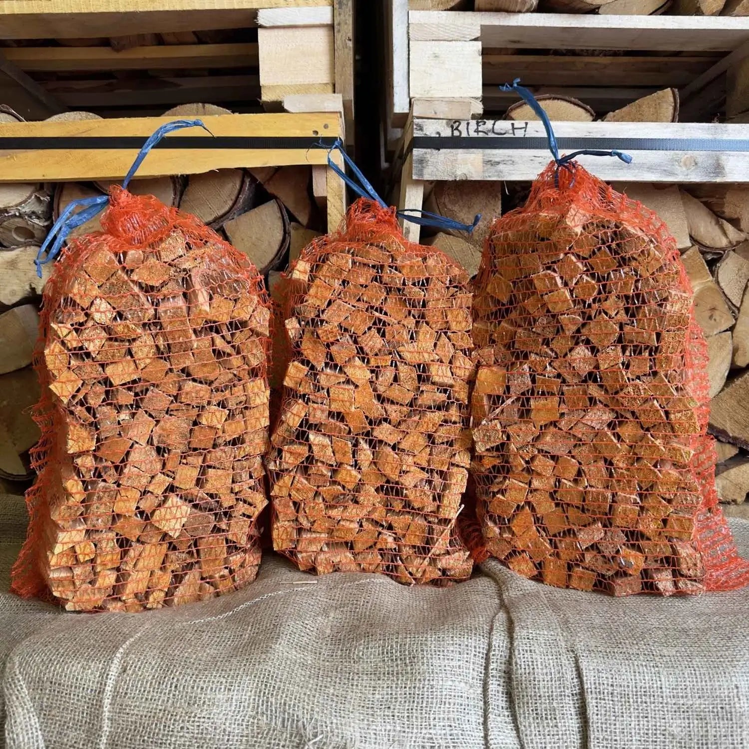 Three bags of firewood stacked on a bale with more firewood in the background.
