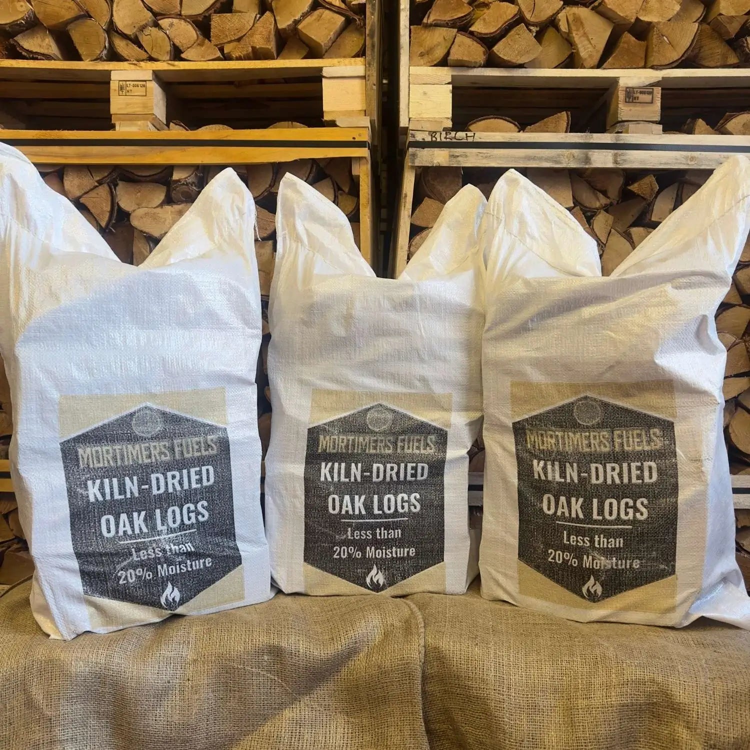 Three bags of Mortimer's Fuels Kiln-Dried Oak Logs with a wooden background.