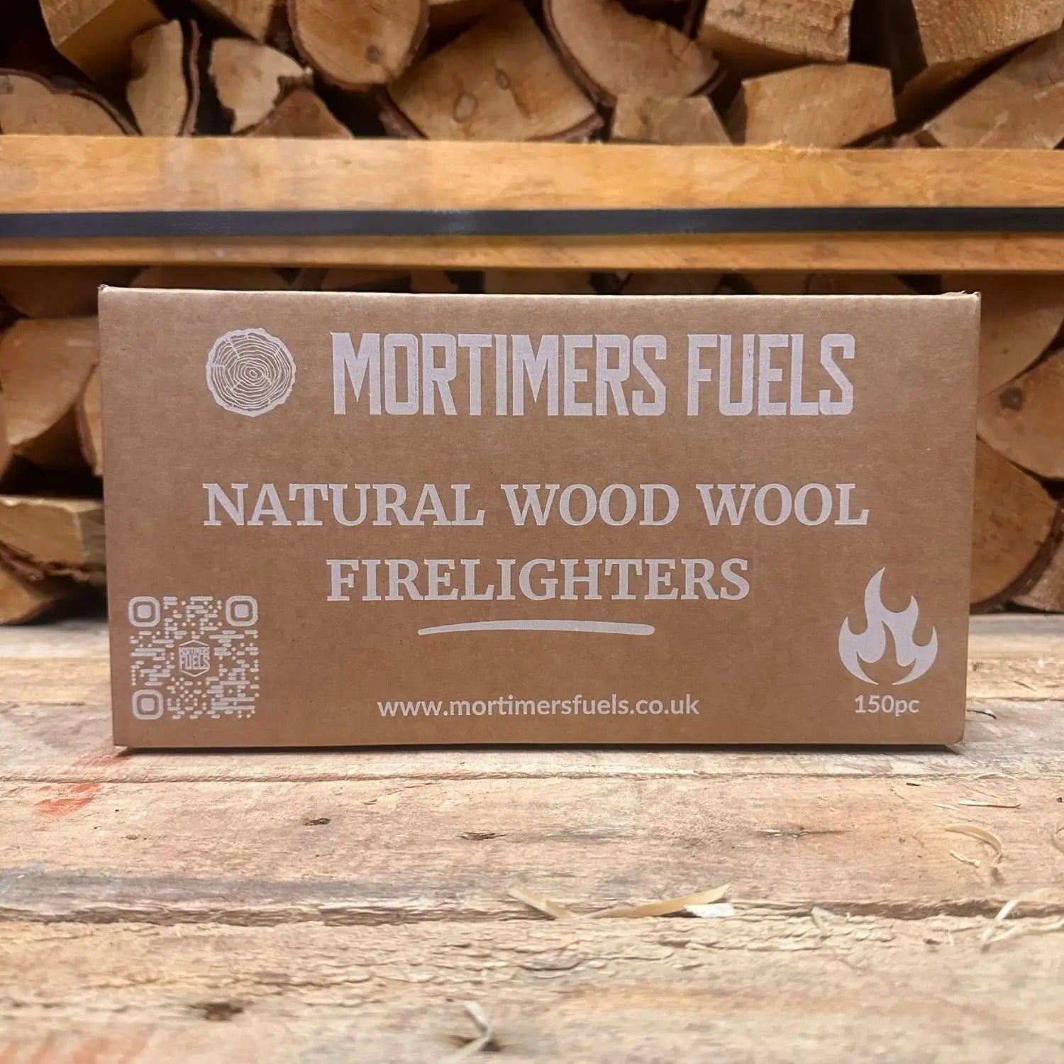 Box of Mortimers Fuels natural wood wool firelighters with stacked logs in the background